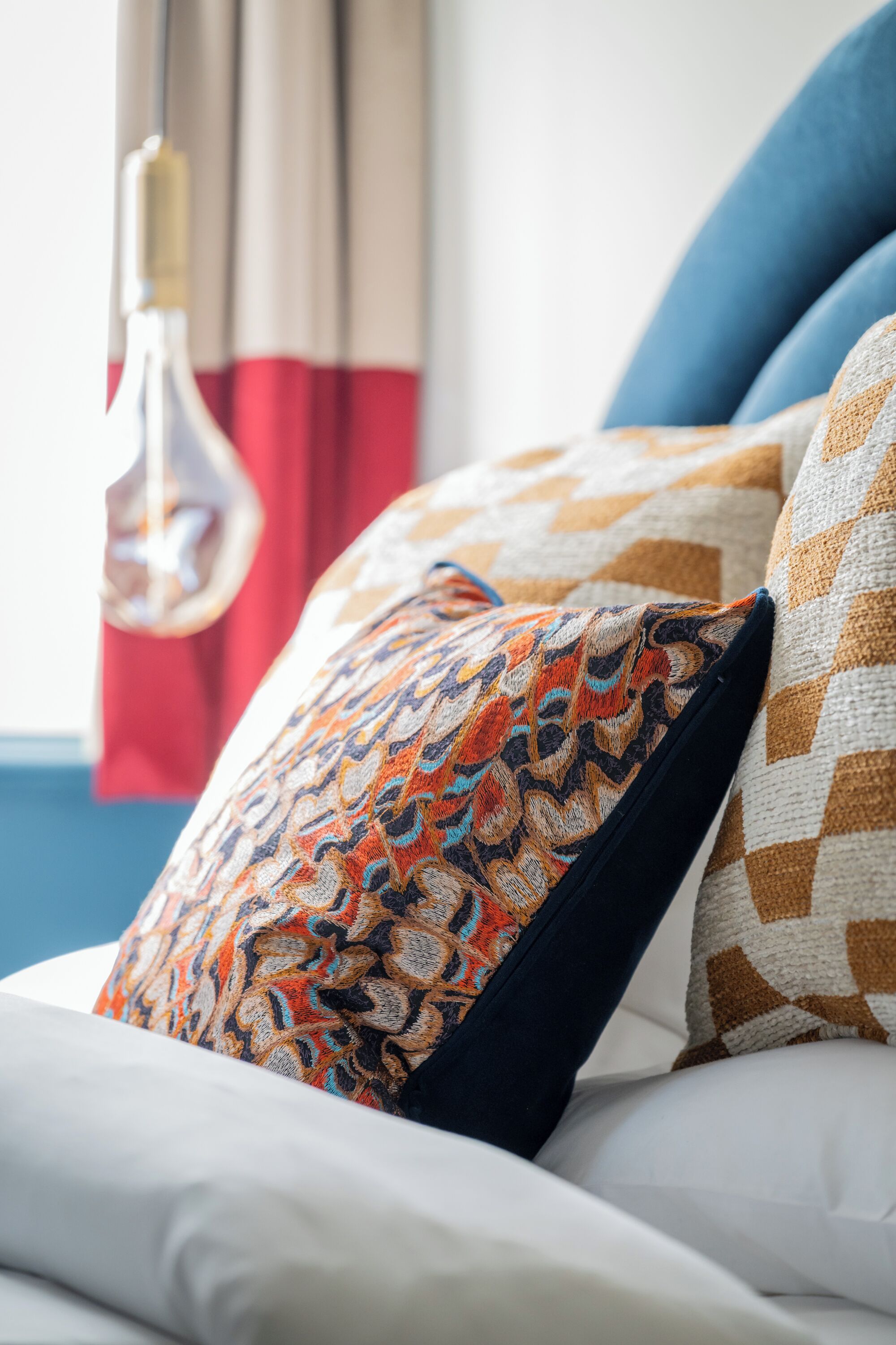 A bed with patterned pillows, a hanging light fixture, and a window with curtains.