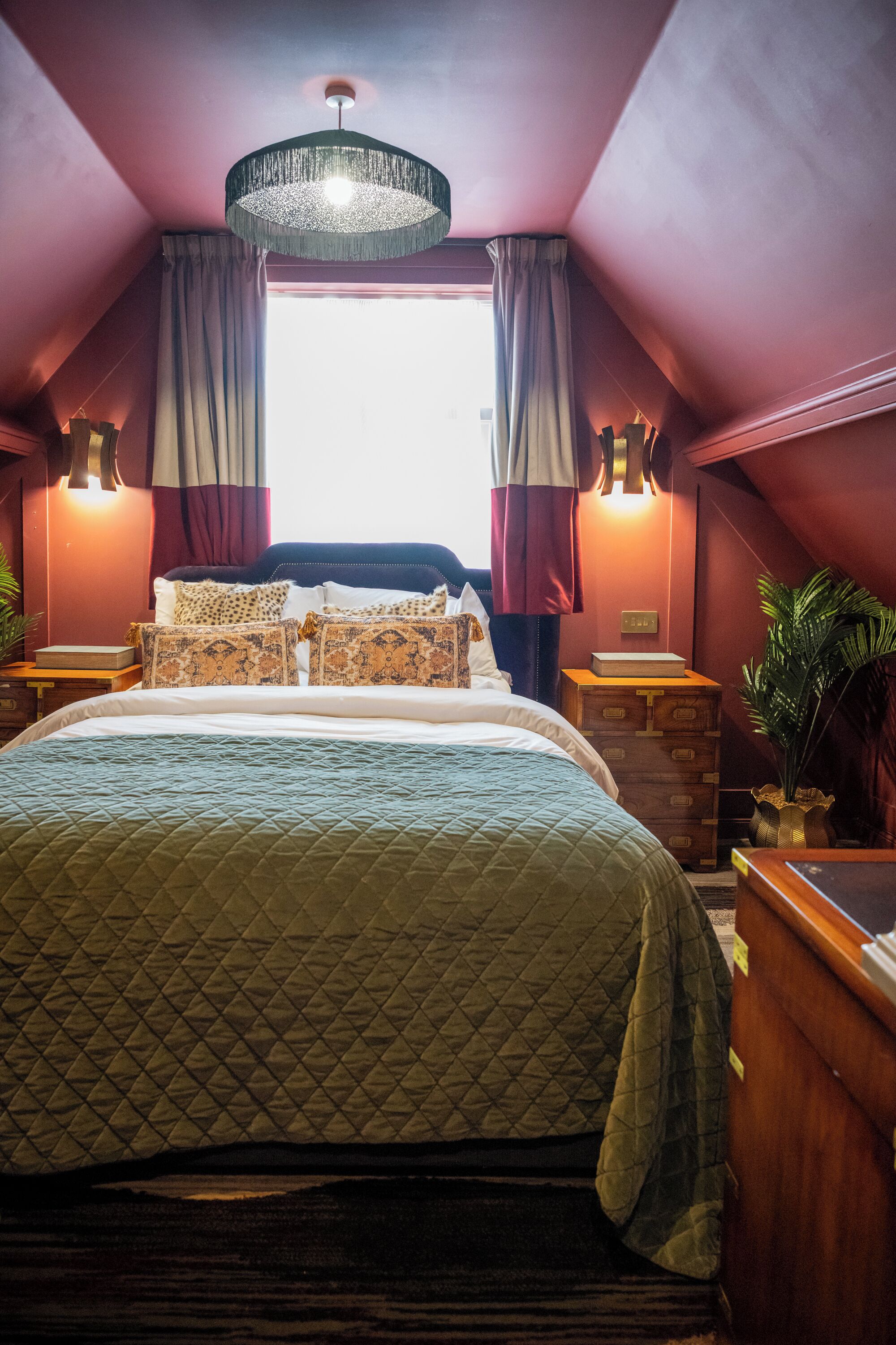 A bedroom with a large bed, a chandelier, curtains, and a window.