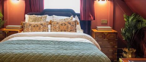 A bedroom with a large bed, a chandelier, curtains, and a window.