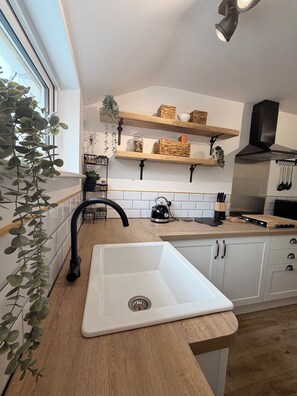 Eine moderne Küche mit einem weißen Spülbecken, Holzregalen und einem schwarzen Wasserhahn.