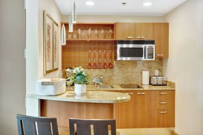 A kitchen with wooden cabinets, a microwave, a toaster, a sink, and a dining area with chairs. - Stylish Studio Hotel at AKA with Free Parking (Miami)