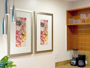 A kitchen with two framed floral paintings, a blender, and a shelf with wine glasses. - Stylish Studio Hotel at AKA with Free Parking (Miami)