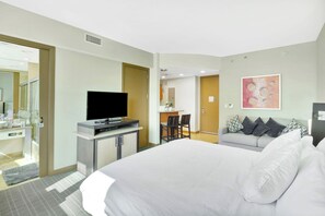 A hotel room with a bed, a television on a stand, a desk with chairs, and a painting on the wall. - Stylish Studio Hotel at AKA with Free Parking (Miami)