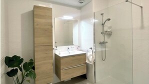 Ein modernes Badezimmer mit Duschkabine aus Glas, Holzwaschtisch und einer Topfpflanze.