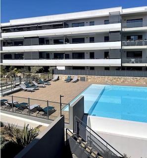 Ein mehrstöckiges Hotel mit Poolbereich auf dem Dach, Liegestühlen und einem klaren, blauen Pool.