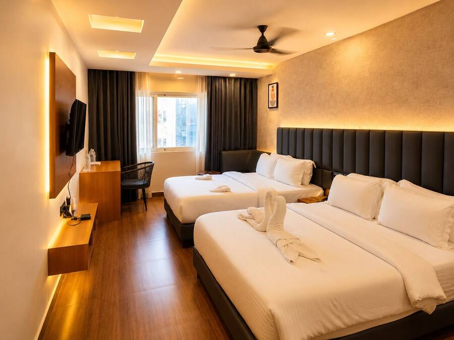 Habitación de hotel con dos camas, un escritorio, una silla, un televisor y un ventilador de techo.