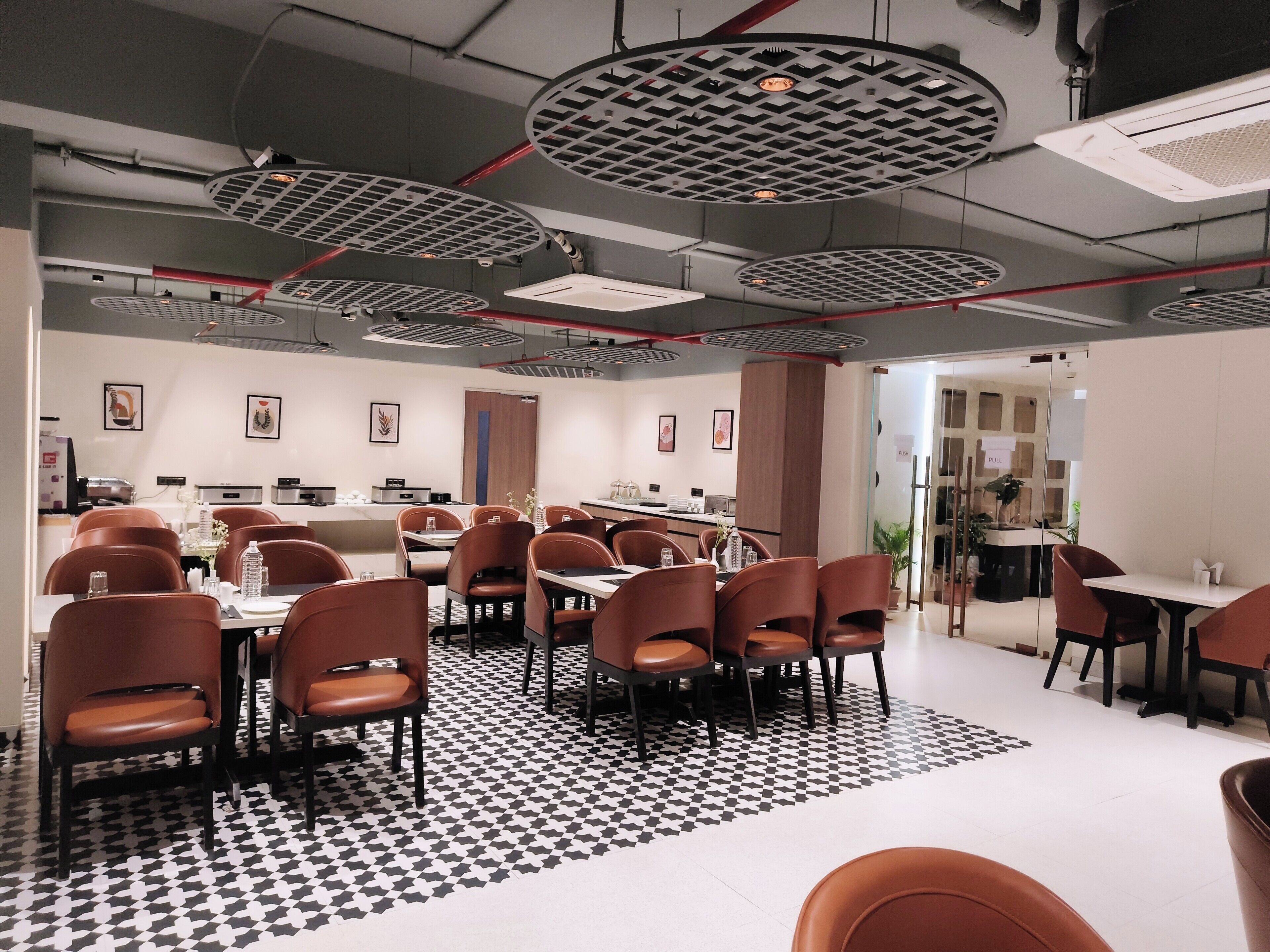 Un comedor moderno con mesas redondas, sillas marrones y suelo estampado.