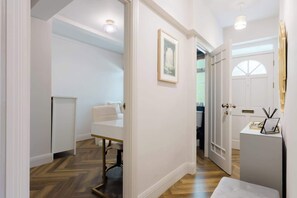 Ein Flur mit einer weißen Tür, einem gerahmten Bild an der Wand und einem weißen Tisch mit einem Stuhl.