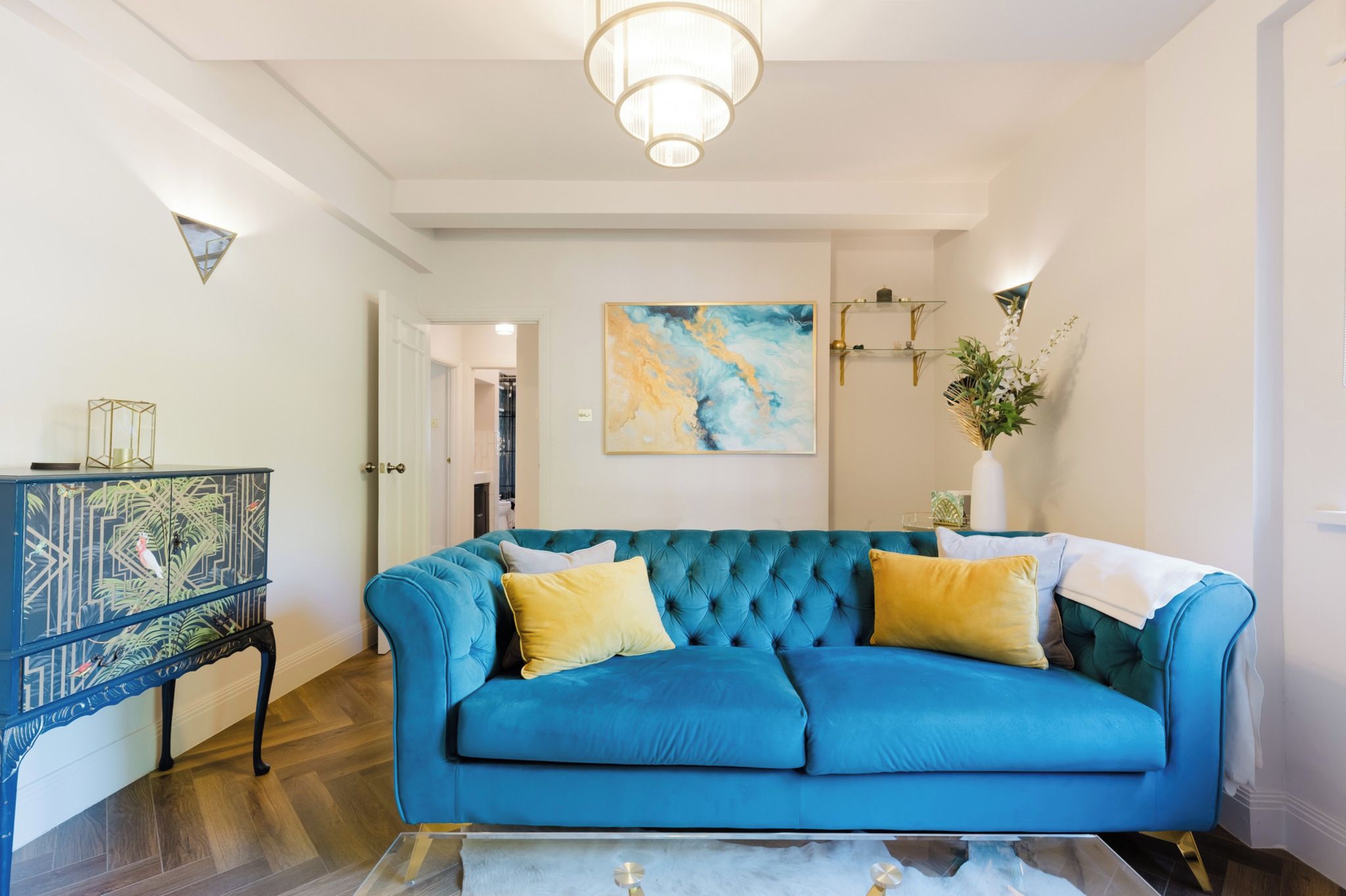 A living room with a blue sofa, decorative pillows, a glass coffee table, and a painting on the wall.