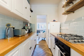 A narrow kitchen with white cabinets, a wooden countertop, a gas stove, and a refrigerator. - Stunning 3BDR Retreat Near Tower Bridge (Greater London)