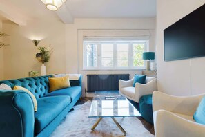 Ein Wohnzimmer mit einer Couch, Sesseln, einem Glastisch, einer Heizung und einem Fenster.