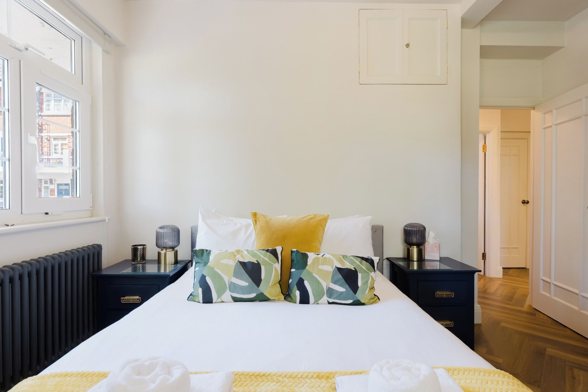 A bedroom with a bed, two bedside tables, a radiator, and a window.