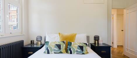 A bedroom with a bed, two bedside tables, a radiator, and a window.