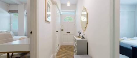 A hallway with a white desk, a bench, a dresser, and a bed in the adjacent room.