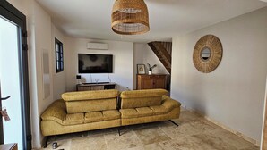 Ein Wohnzimmer mit einer Couch, einem Fernseher, einer Weiden-Deckenleuchte, einem Holzschrank und einer Treppe.