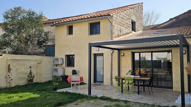 Ein Haus mit Terrasse, überdachter Sitzgelegenheit und einer Tür, die zu einer Garage führt.