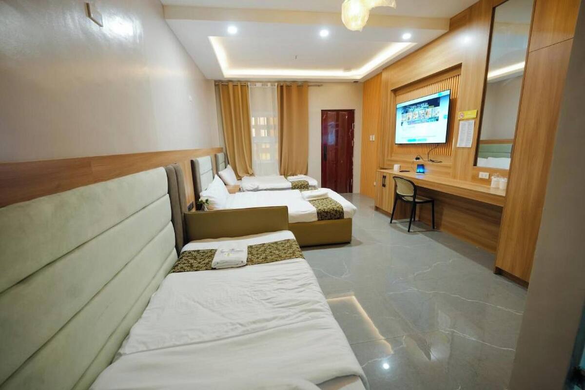 Habitación de hotel con tres camas, un escritorio, un televisor y un espejo.