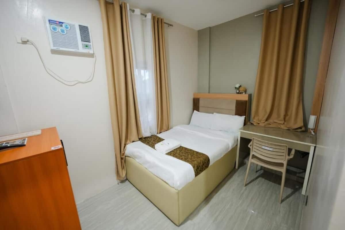 Una habitación de hotel con cama, escritorio, silla y un equipo de aire acondicionado en la pared.