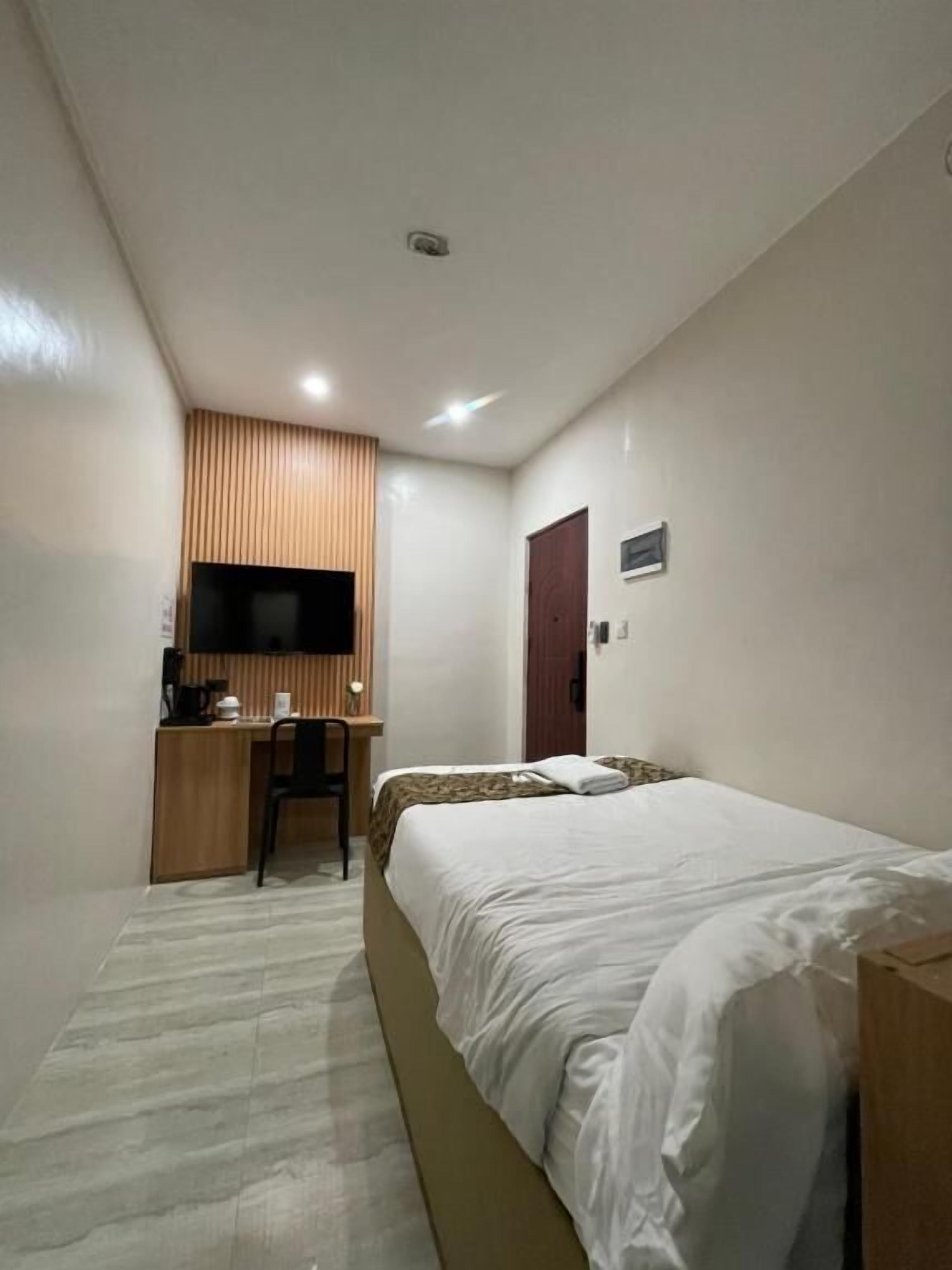 Une chambre d’hôtel avec un lit, un bureau, une chaise, une télévision et une porte.