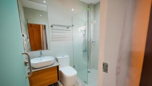 A modern bathroom with a glass shower enclosure, a white sink, and a wooden vanity. - Casa Familia Hotel (Aurora)