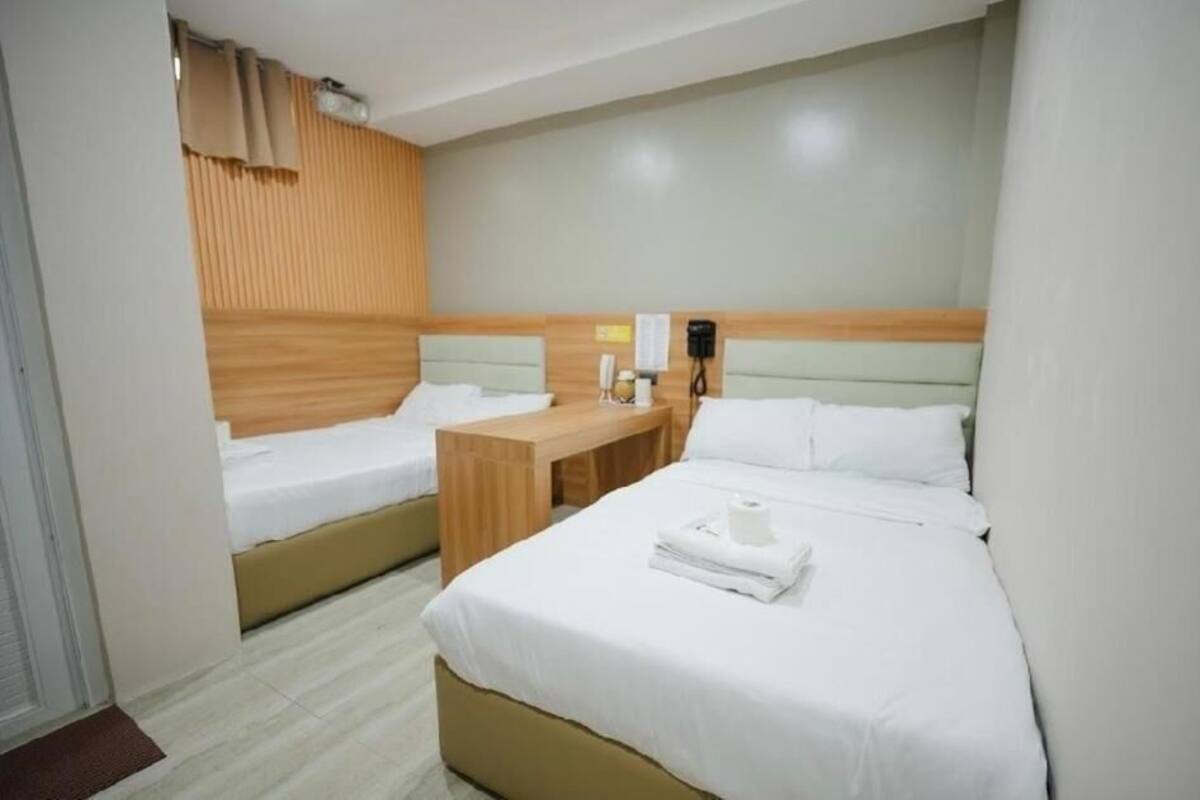 Habitación de hotel con dos camas, cabecero de madera, mesita de noche con teléfono y luz de pared.