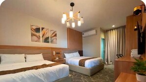 A hotel room with two beds, a desk, a chair, a plant, artwork on the wall, and a chandelier. - Casa Familia Hotel (Aurora)