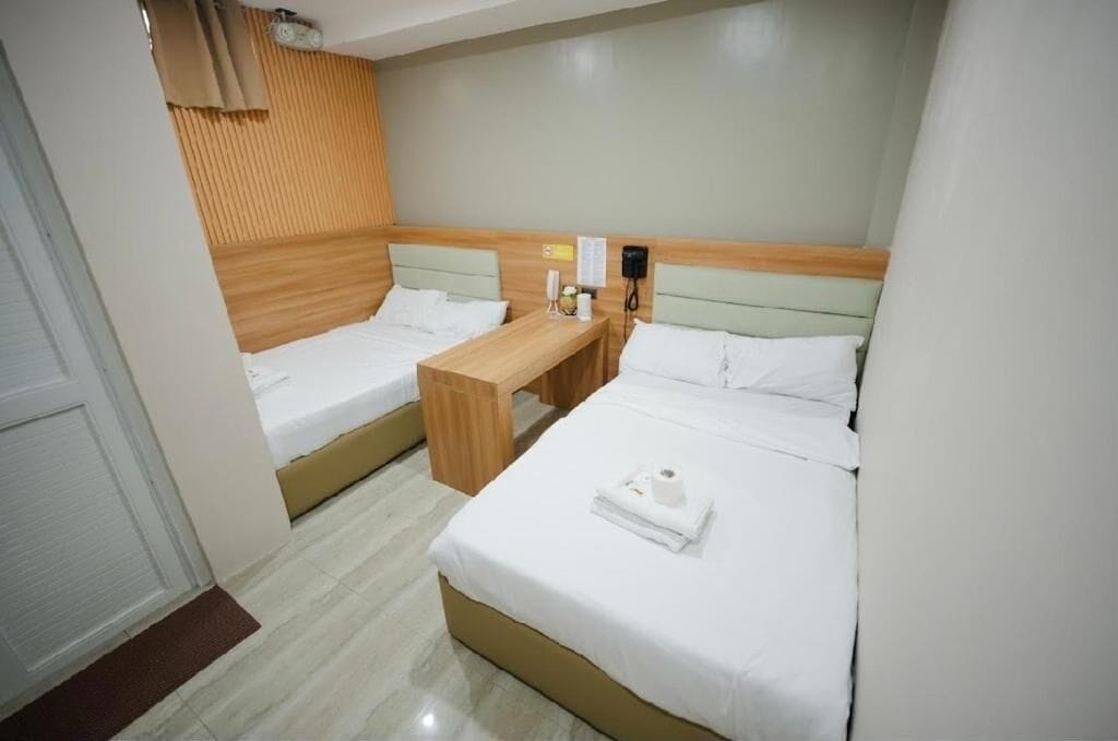 A hotel room with two beds, a wooden nightstand, a telephone, and a wall-mounted light.