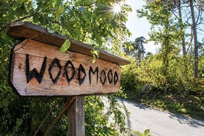 A wooden sign with the name 'WOODMOOD' in a rustic style, surrounded by greenery and a road. - WOODMOOD tent with wellness (Leuk)