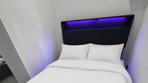 Un lit moderne avec une tête de lit, du linge de lit blanc et une moquette foncée.