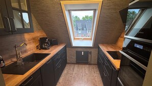 Une cuisine compacte avec des meubles de couleur sombre, un plan de travail en bois, un four Bosch et un puits de lumière.