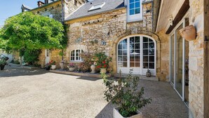 A stone building with a gravel driveway, large windows, and potted plants. - Gîte "Le Four à Pain" – Charming Studio with Private Terrace in Périgord Noir (Paulin)