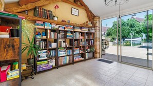 A library with bookshelves, a chandelier, and a view of the outside. - Gîte "Le Four à Pain" – Charming Studio with Private Terrace in Périgord Noir (Paulin)