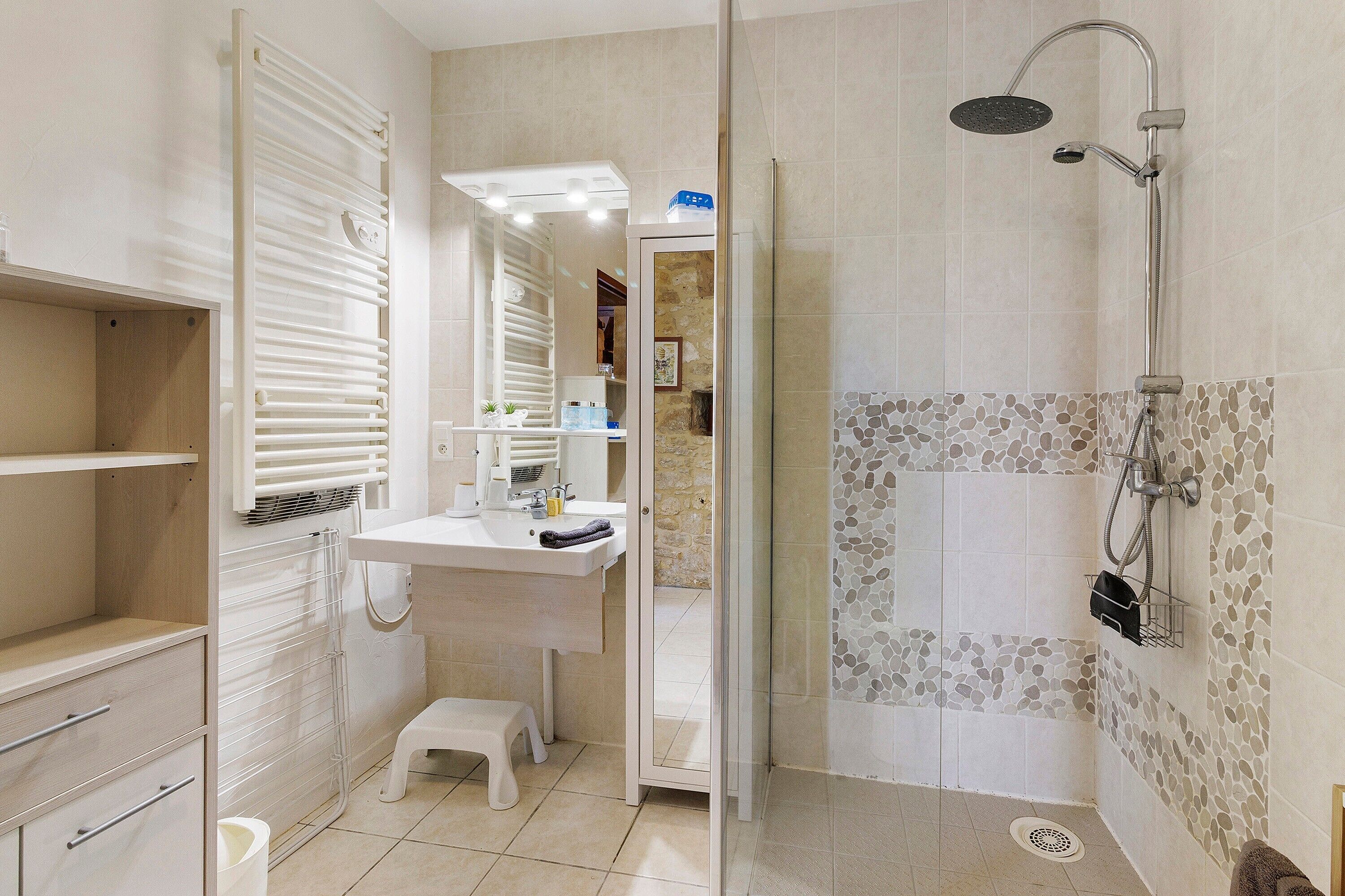Een badkamer met een douche, toilet, wastafel en een klein opstapkrukje.