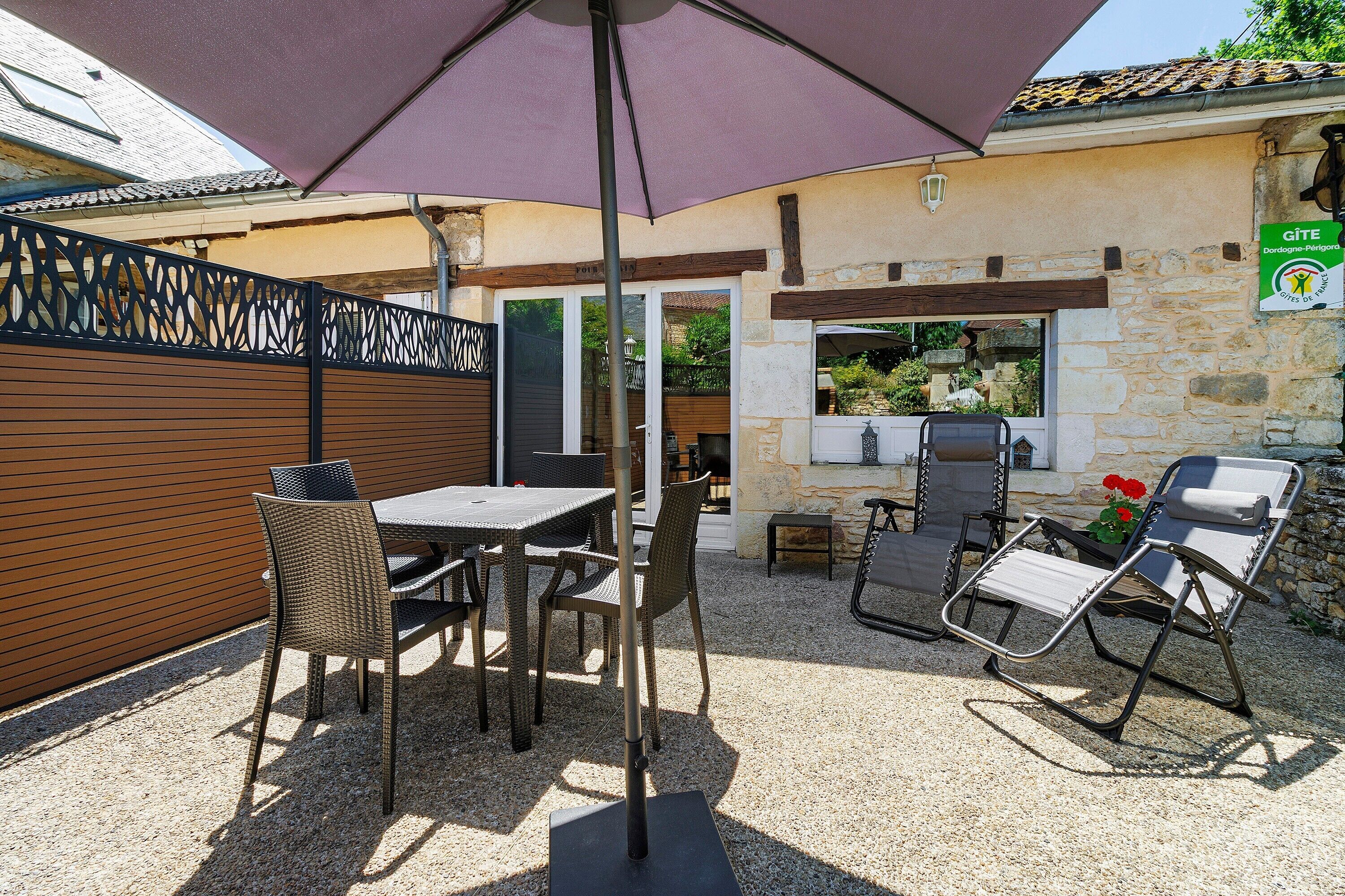 An outdoor patio with a table and chairs, a pergola, and a stone wall.