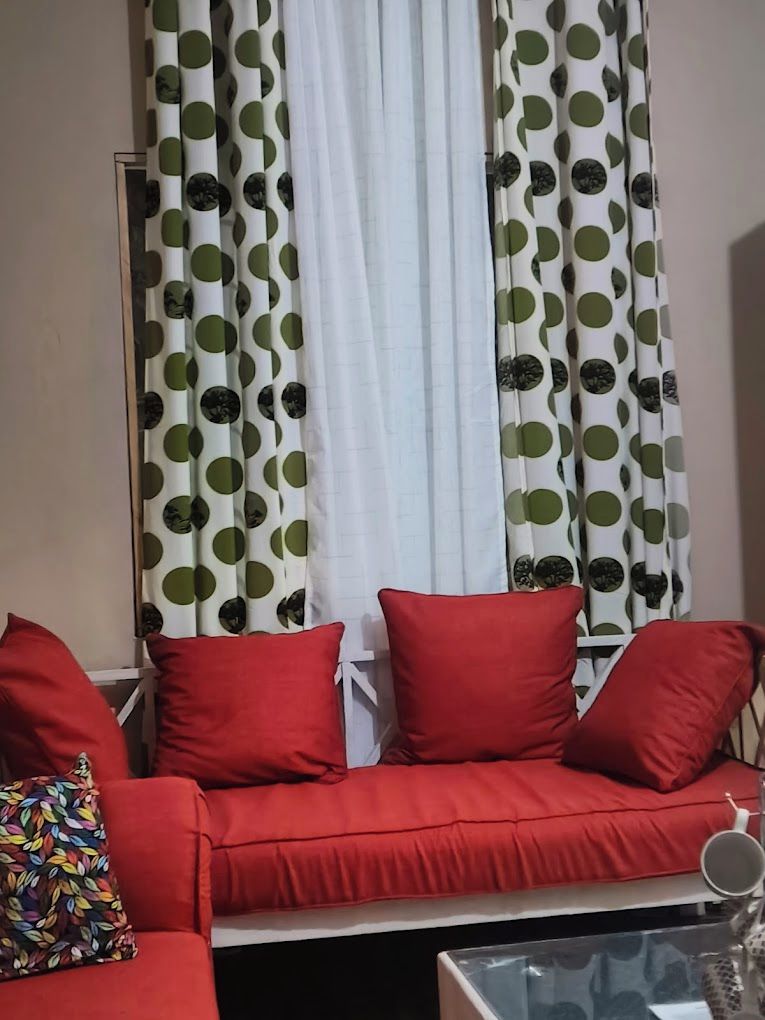 A living room with a red sofa, a glass coffee table, and curtains with a green and white pattern.