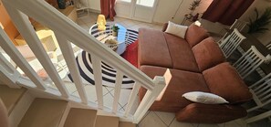 Un escalier mène à un salon où se trouvent un canapé marron, une table basse ronde et un tapis à rayures.
