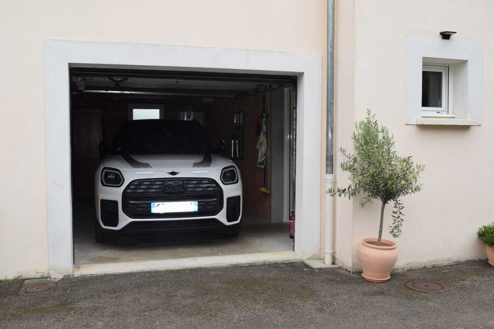 A white car parked in a garage with a potted plant beside it.