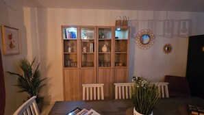 Un comedor con un aparador de madera, sillas blancas, una mesa con revistas y una planta en maceta.