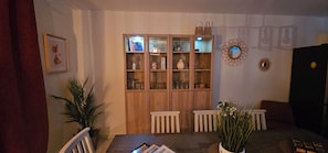 Un coin repas comprenant un buffet en bois, des chaises blanches, une table avec des magazines et une plante en pot.