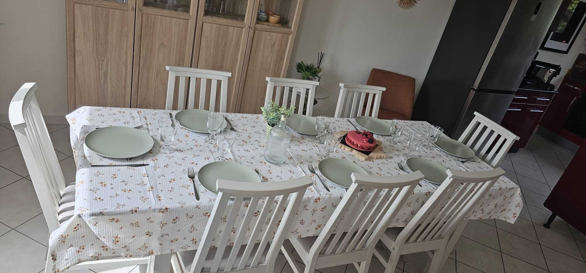 A dining table set with plates, glasses, and cutlery, surrounded by white chairs.
