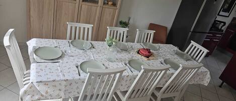 A dining table set with plates, glasses, and cutlery, surrounded by white chairs.