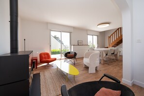 A modern living room with a fireplace, a dining area with a table and chairs, and a staircase leading to an upper level.
