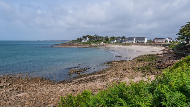 Et kystlandskab med en stenstrand, række af huse og en klar himmel.
