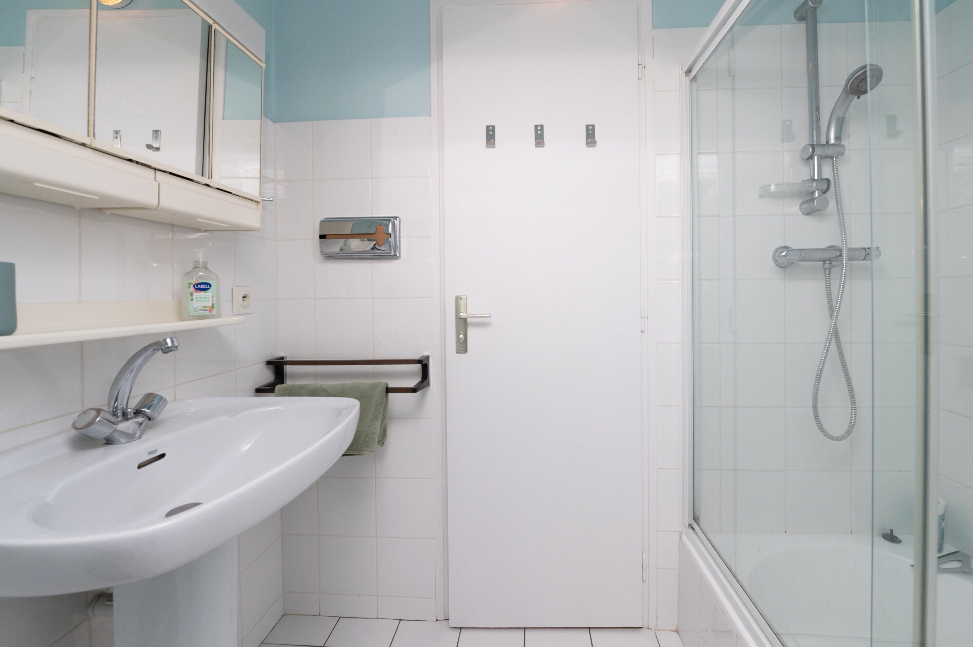 A bathroom with a white sink, a glass shower enclosure, and a door with a towel rack.
