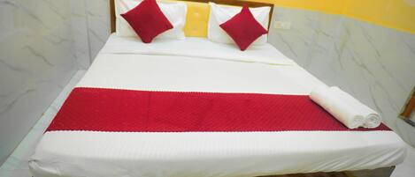 Una cama con colchón blanco, almohadas rojas y blancas, y una manta roja.