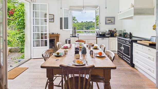 Un comedor con una mesa de madera, sillas y vistas al exterior con vegetación.