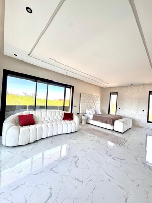 Ein modernes Wohnzimmer mit einem Ecksofa, einem Bett und einem großen Fenster mit Blick auf Grünflächen.