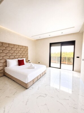 Ein modernes Schlafzimmer mit einem großen Bett, einem markanten, geometrischen Kopfteil und einer Glastür, die auf einen Balkon führt.