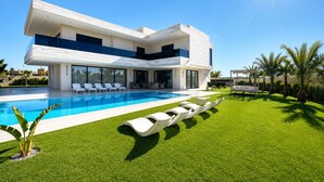 Een modern huis met twee verdiepingen, een zwembad, een verzorgd gazon en een pergola.