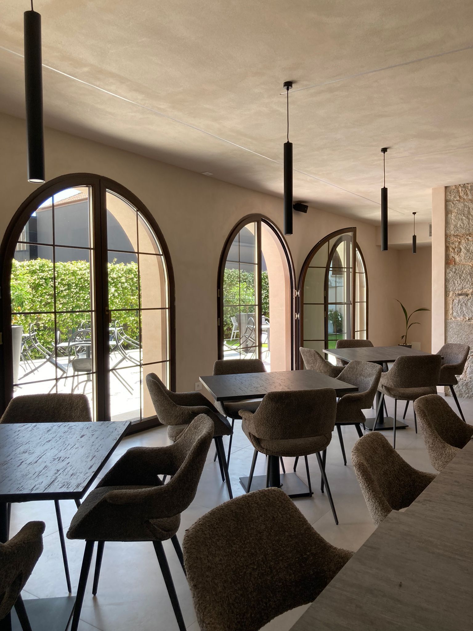 A modern dining area with arched windows, tables, chairs, and pendant lights.